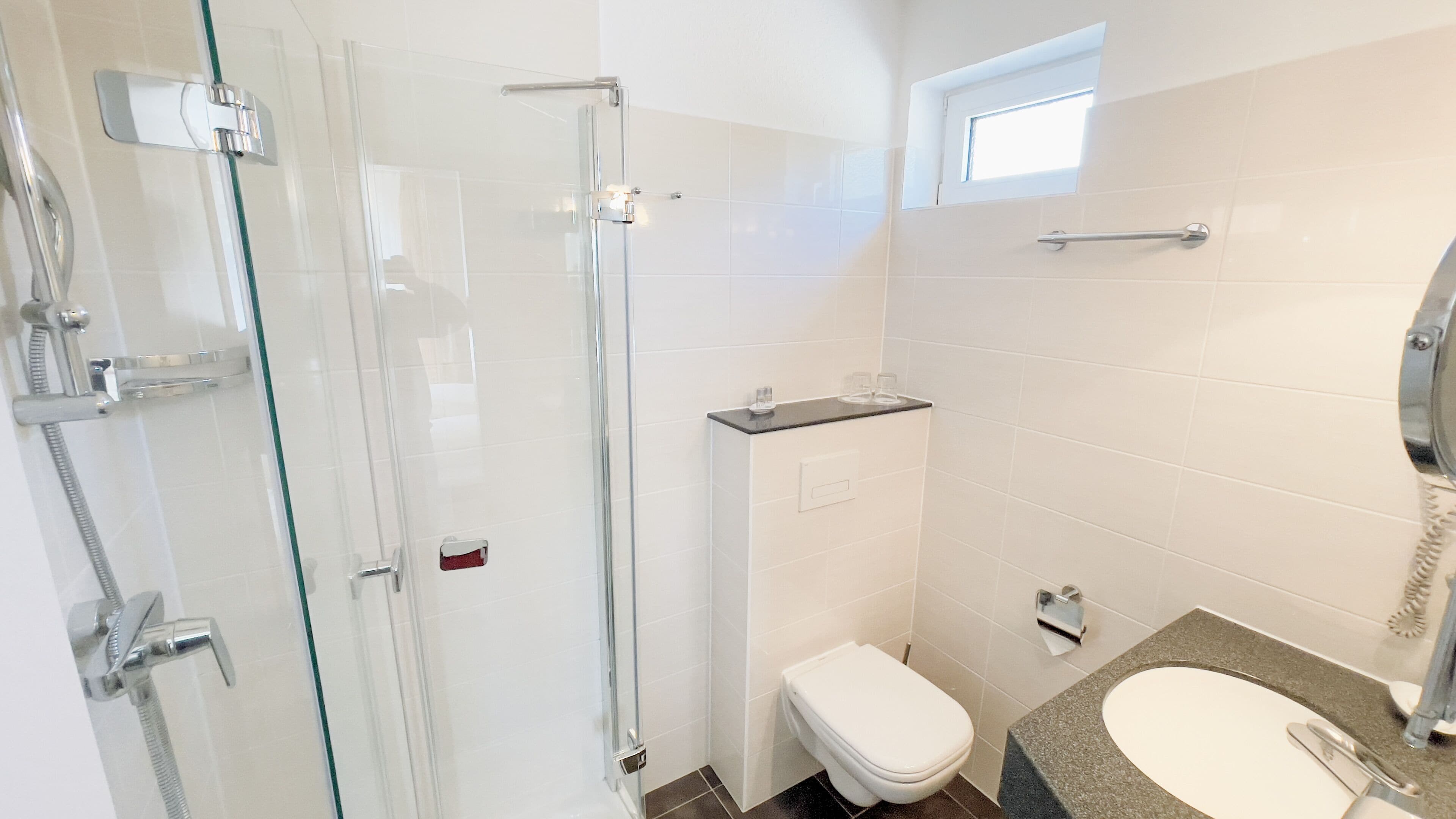 A modern bathroom with a glass shower enclosure, a toilet, and a sink with a telephone.