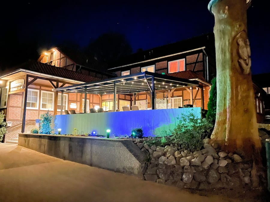 Un edificio a due piani con un patio coperto, un muro in pietra e un grande albero sullo sfondo.