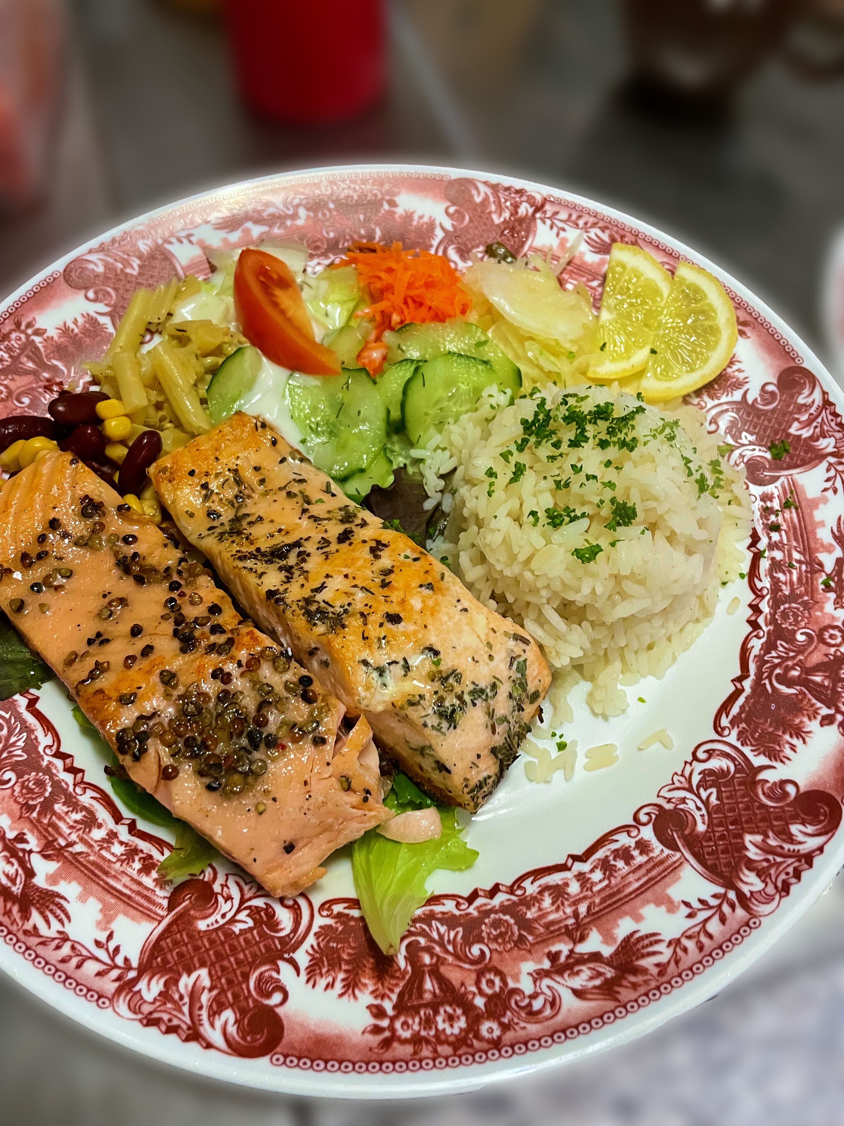 A plate with salmon, rice, vegetables, and lemon slices.