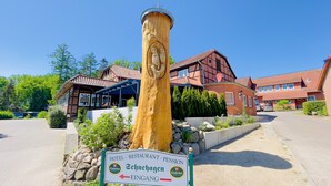 A wooden post with carved owls, a sign indicating hotel, restaurant, and pension services, and a view of traditional buildings. - Hotel Schnehagen (Bad Fallingbostel)