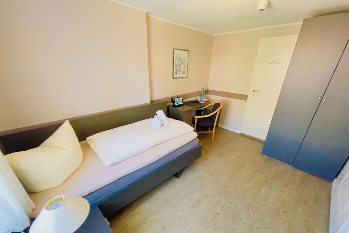 Quarto de hotel com uma cama, uma escrivaninha, uma cadeira e um guarda-roupa.