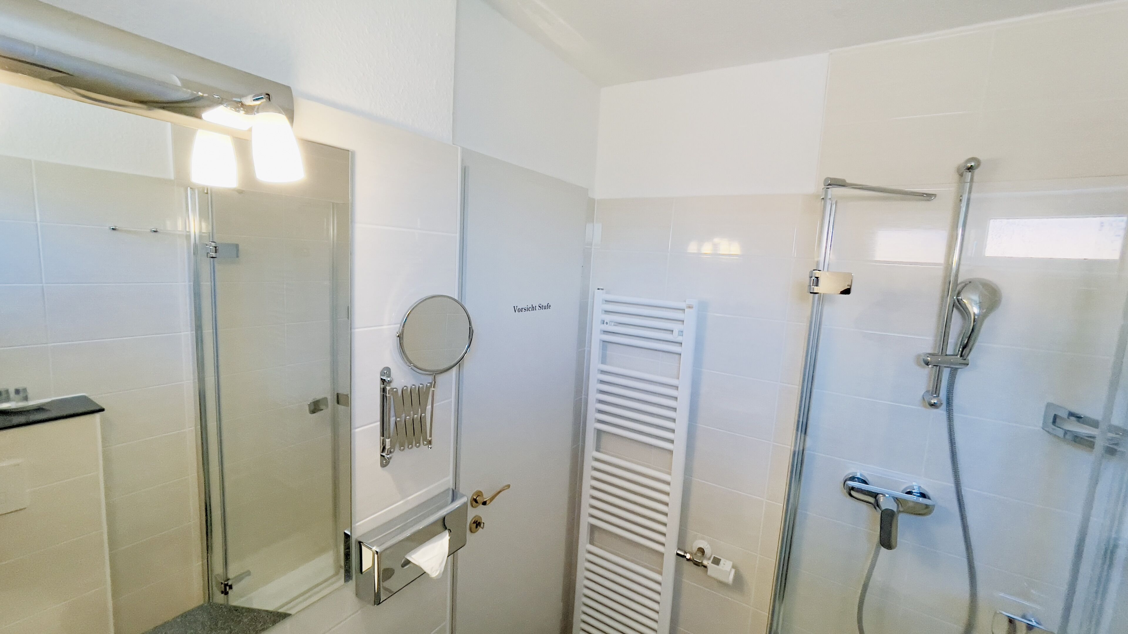 Un baño moderno con cabina de ducha de vidrio, un perchero, un inodoro y un espejo.