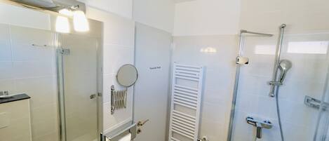 Un baño moderno con cabina de ducha de vidrio, un perchero, un inodoro y un espejo.