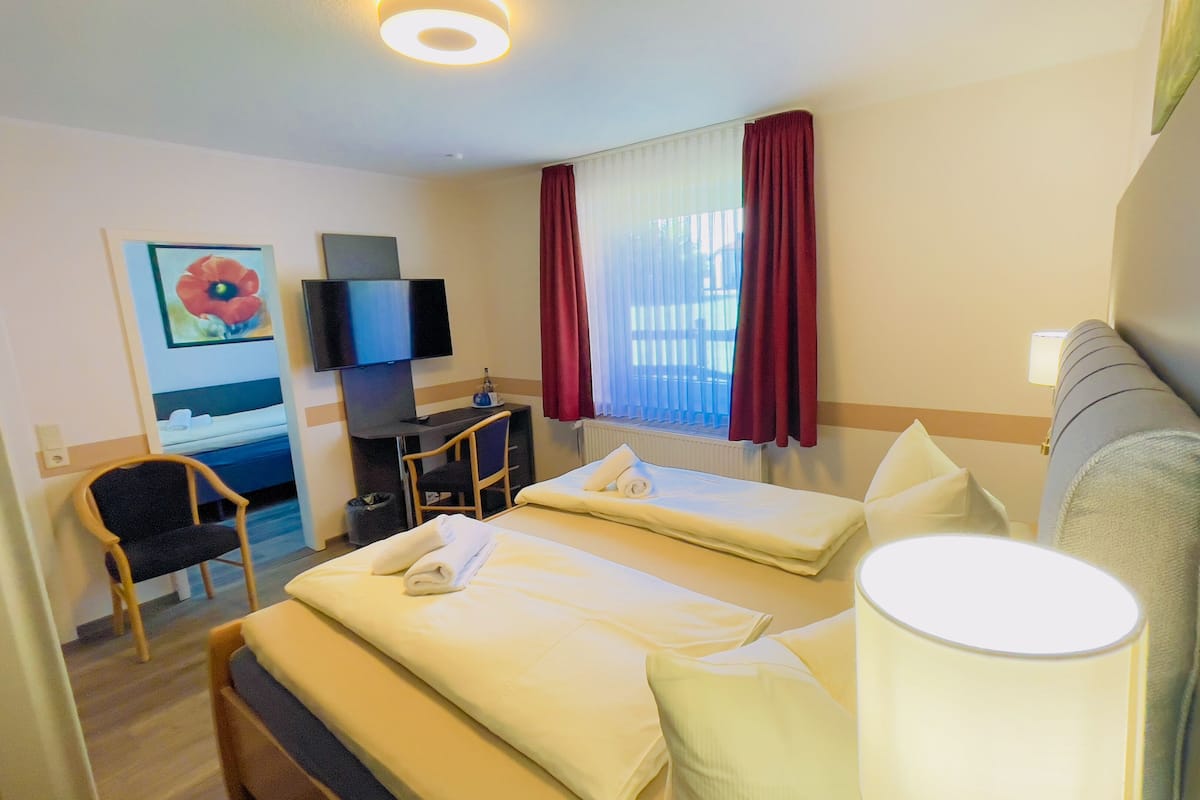 Quarto de hotel com cama, escrivaninha, cadeira, televisão e janela com cortinas.