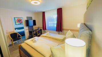 Quarto de hotel com cama, escrivaninha, cadeira, televisão e janela com cortinas.