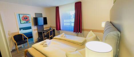 Una habitación de hotel con cama, escritorio, silla, televisor y ventana con cortinas.