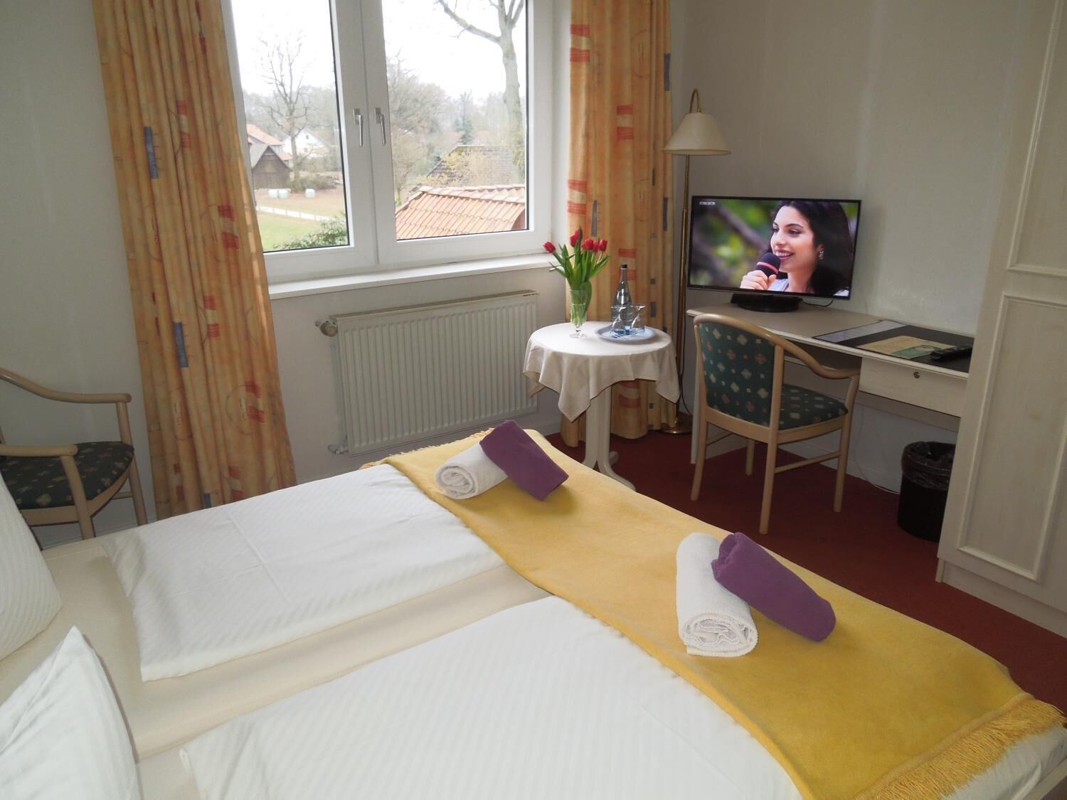 Habitación de hotel con cama, escritorio con computadora, televisor y ventana con cortinas.