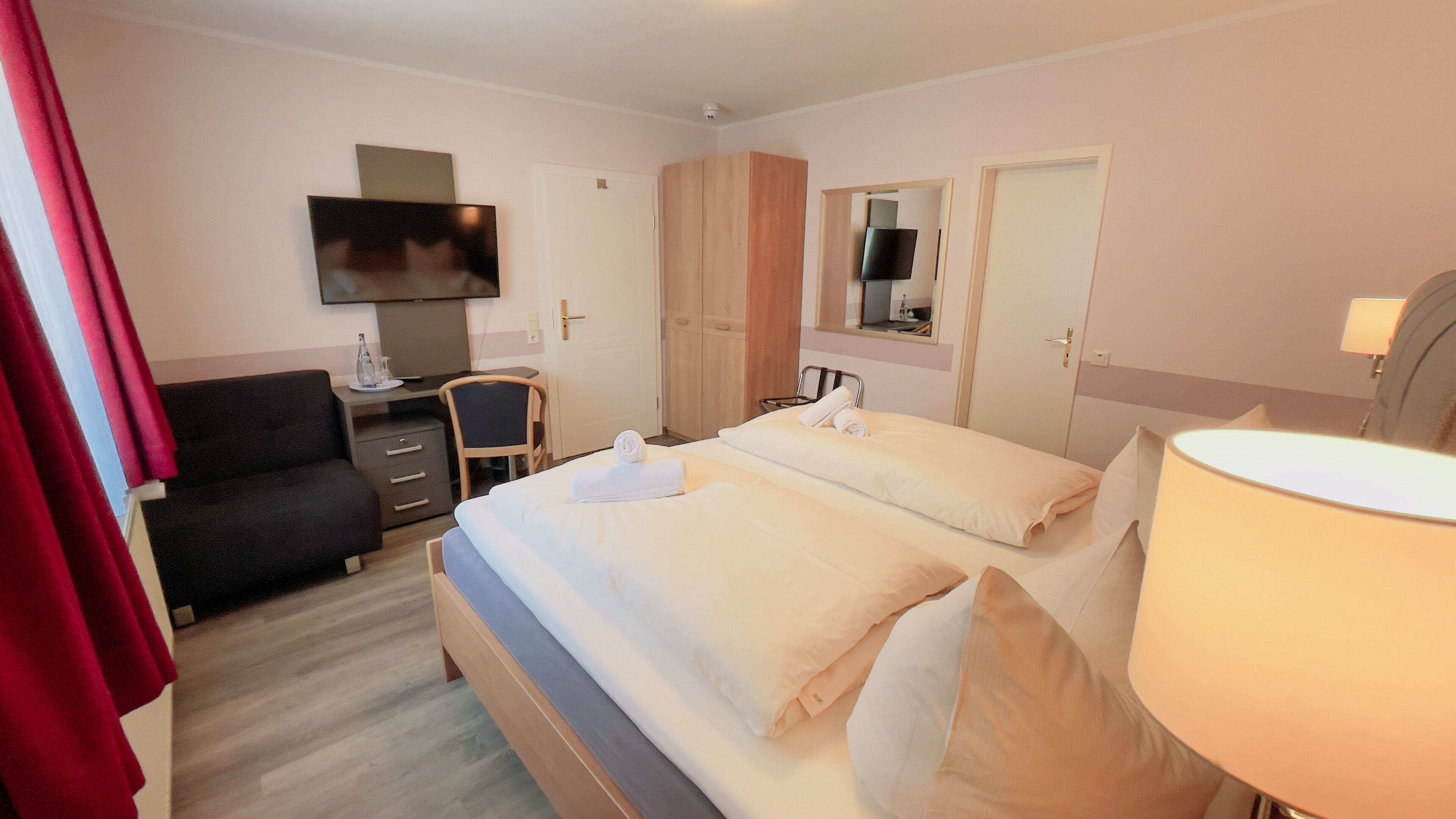 A hotel room with a bed, a desk, a chair, a TV, and a wardrobe.