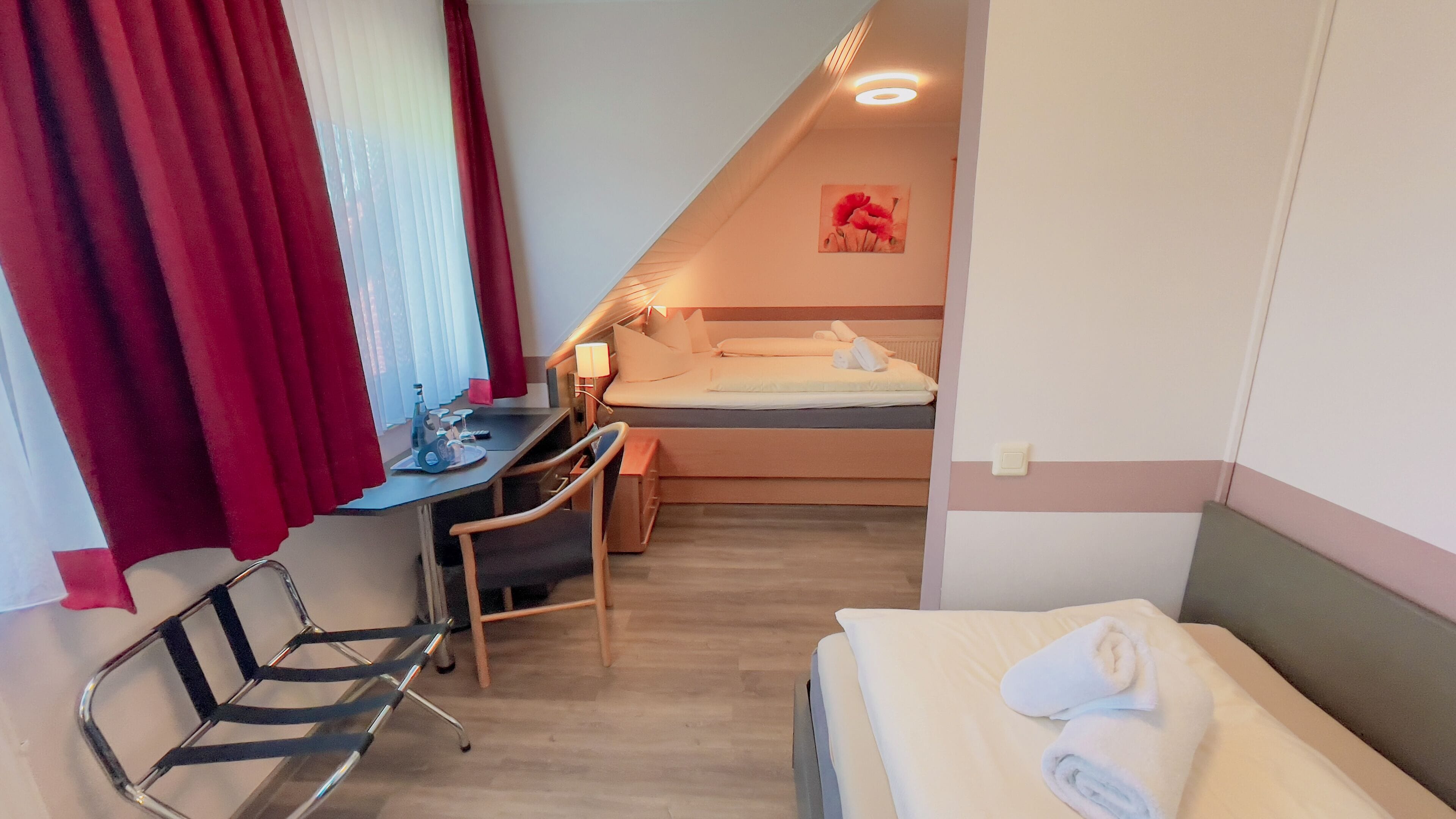 Una habitación de hotel compacta con cama, escritorio, silla y una pequeña mesa.