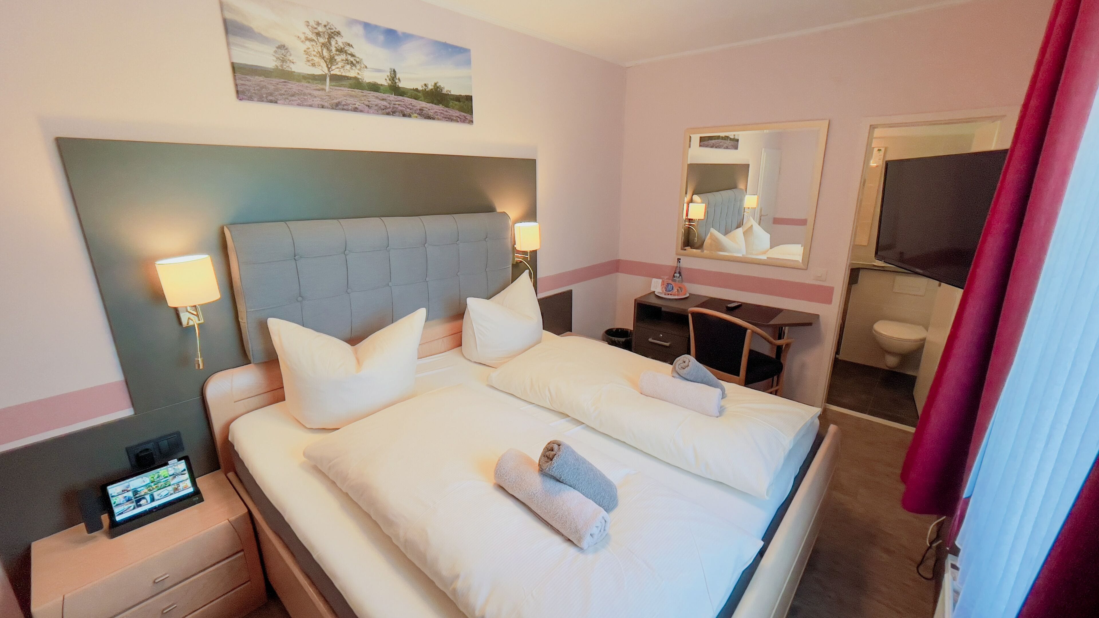 A hotel room with a large bed, two bedside tables, a desk, a chair, a mirror, and a bathroom.