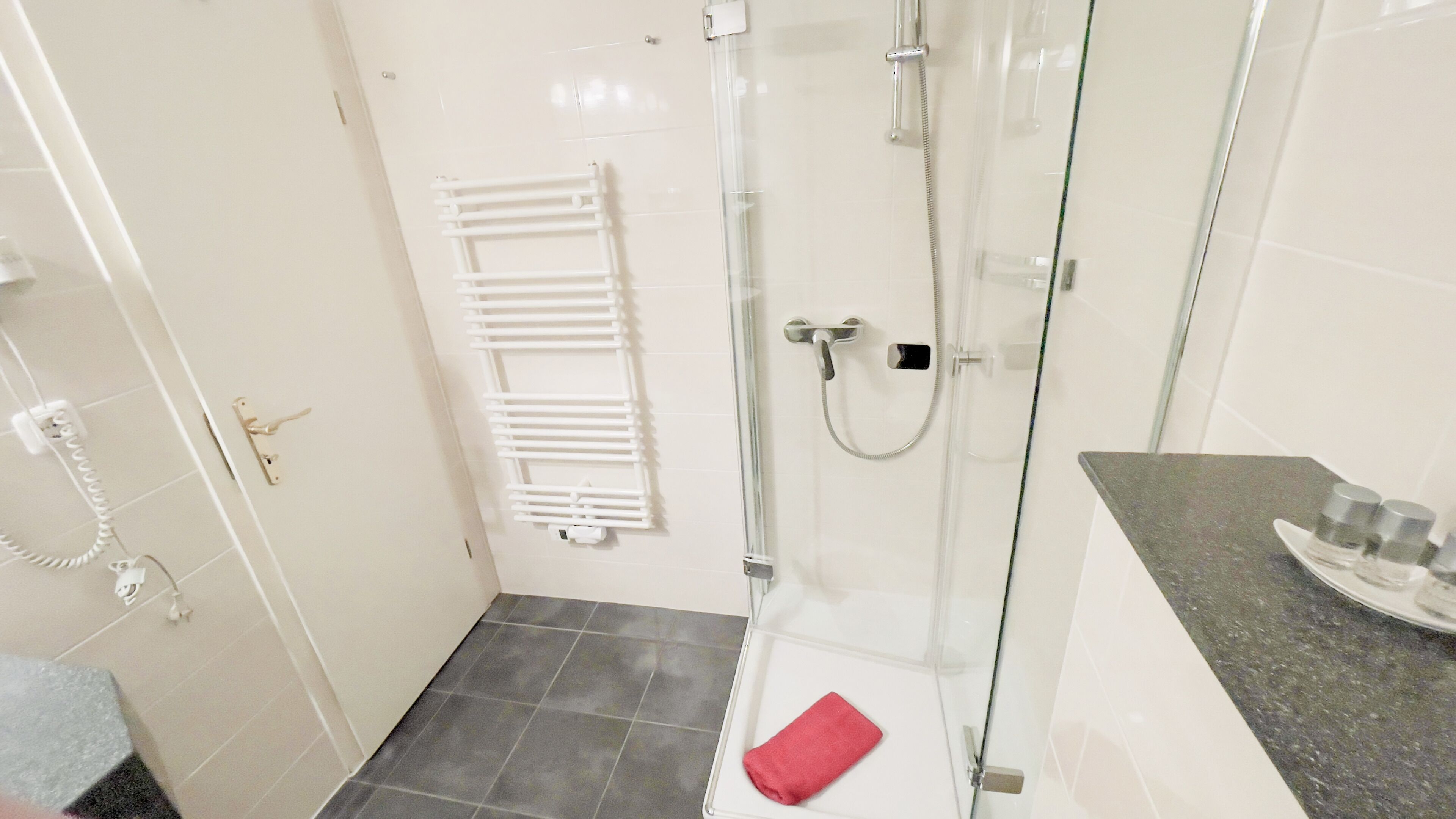 A bathroom with a glass-enclosed shower, a white towel on the floor, and a towel rack on the wall.