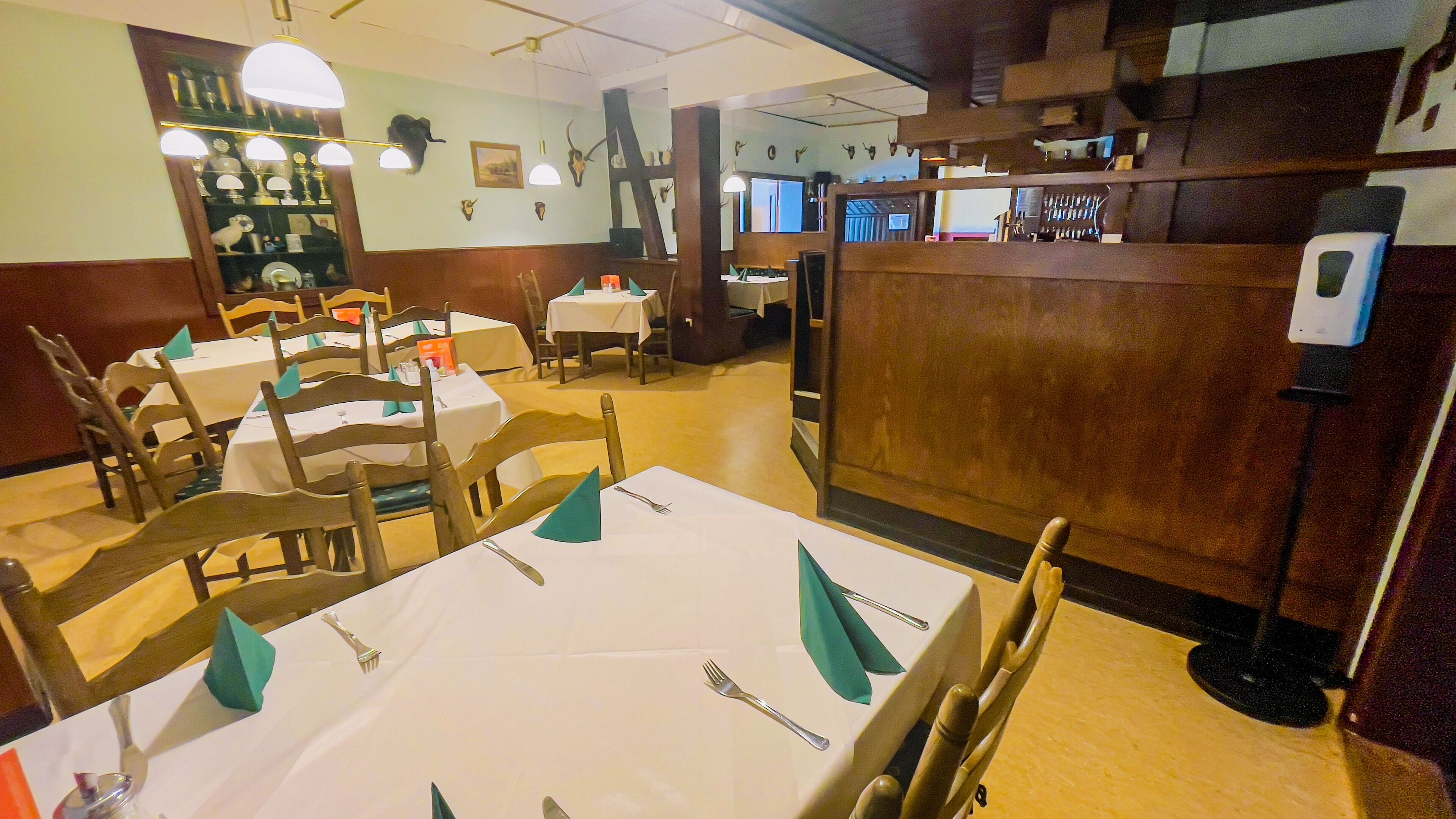 Interior de restaurante con varias mesas listas para comer, sillas de madera y diversas decoraciones en las paredes, incluyendo cuernos de animales y cuadros enmarcados.