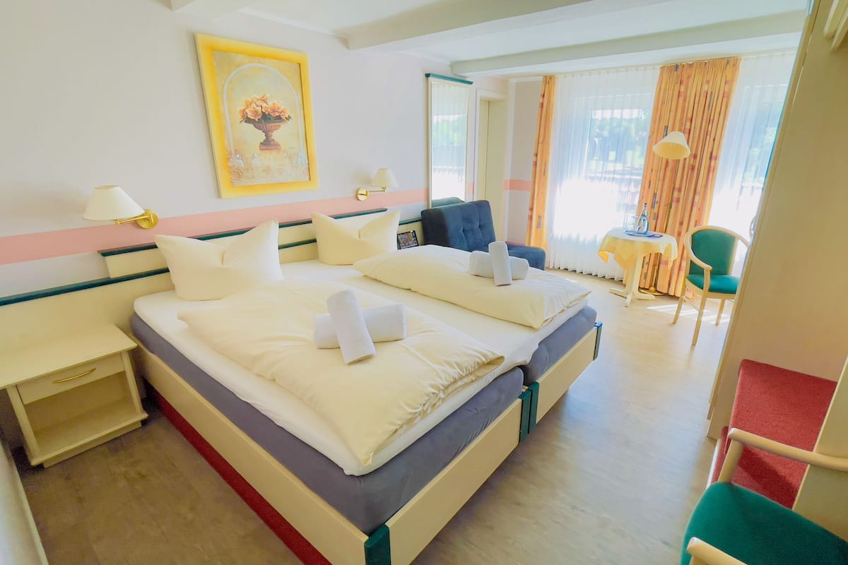 Quarto de hotel com duas camas, uma escrivaninha, uma cadeira e uma mesa com abajur.