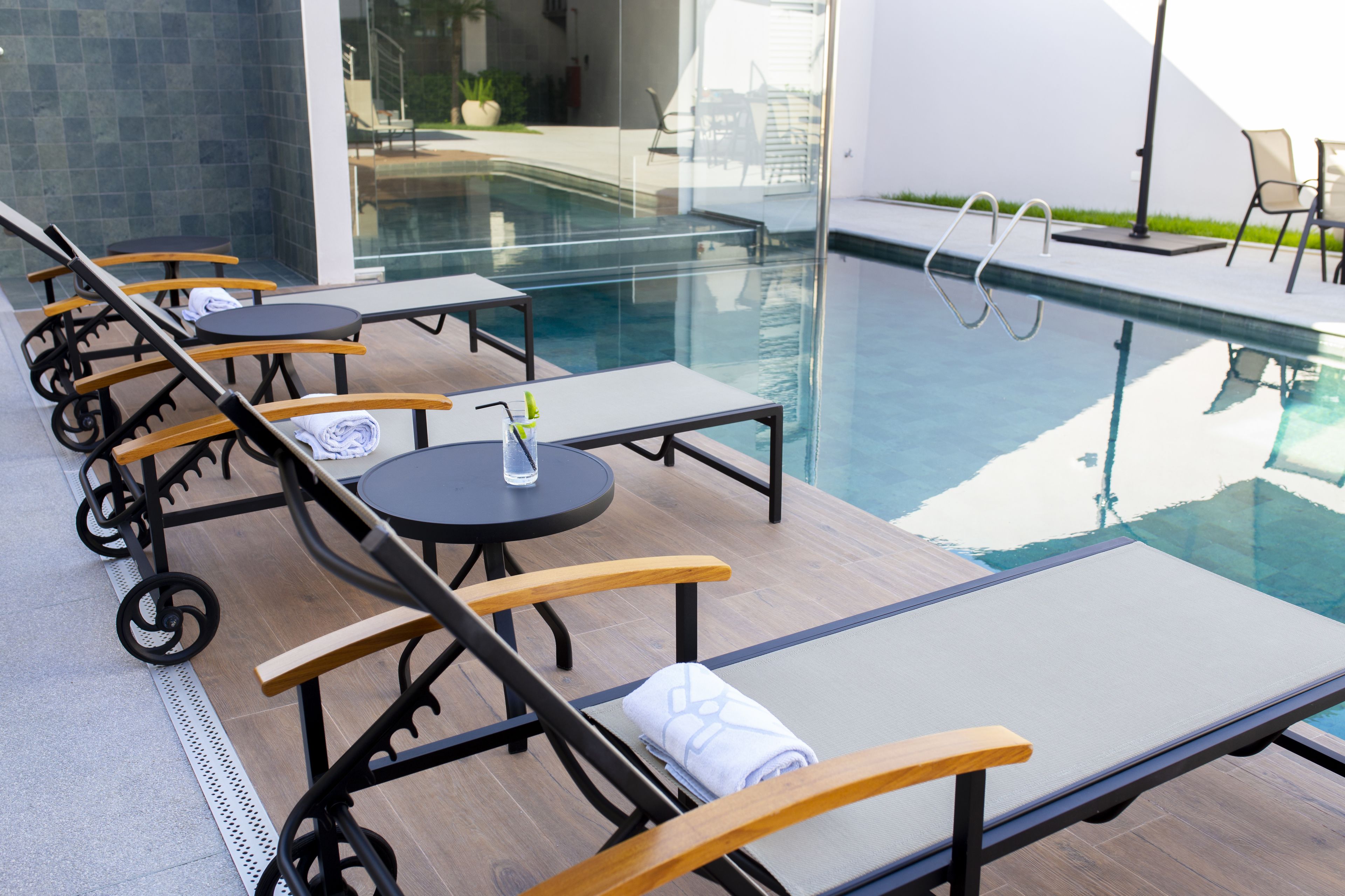 A poolside area with lounge chairs and tables, a clear pool, and a modern building in the background.