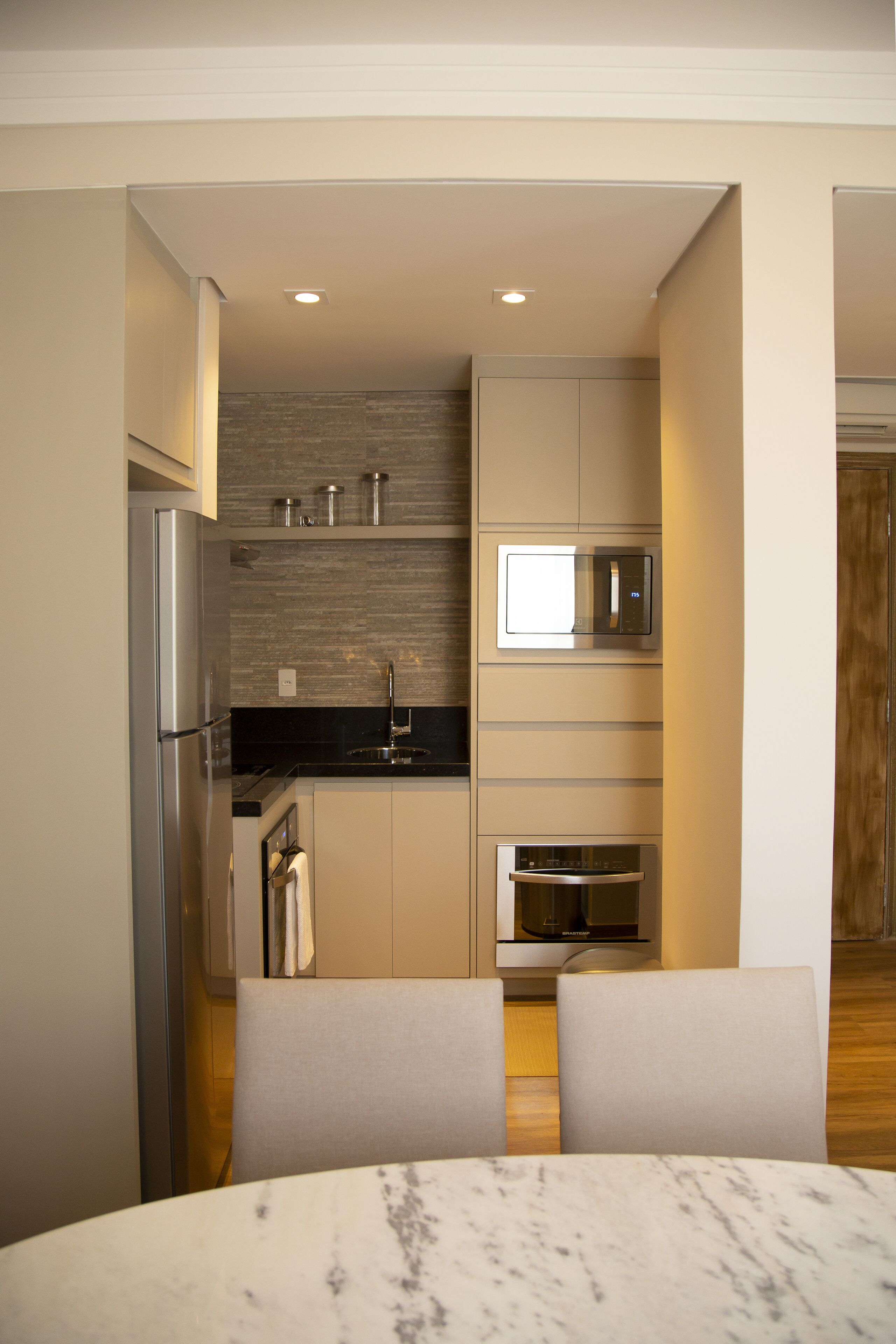 A compact kitchen with a refrigerator, microwave, oven, and a dining area with a marble table.