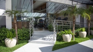 A modern building with a glass facade, a staircase leading to the entrance, and potted plants around the entrance area. - Hotel Florença (Americana)