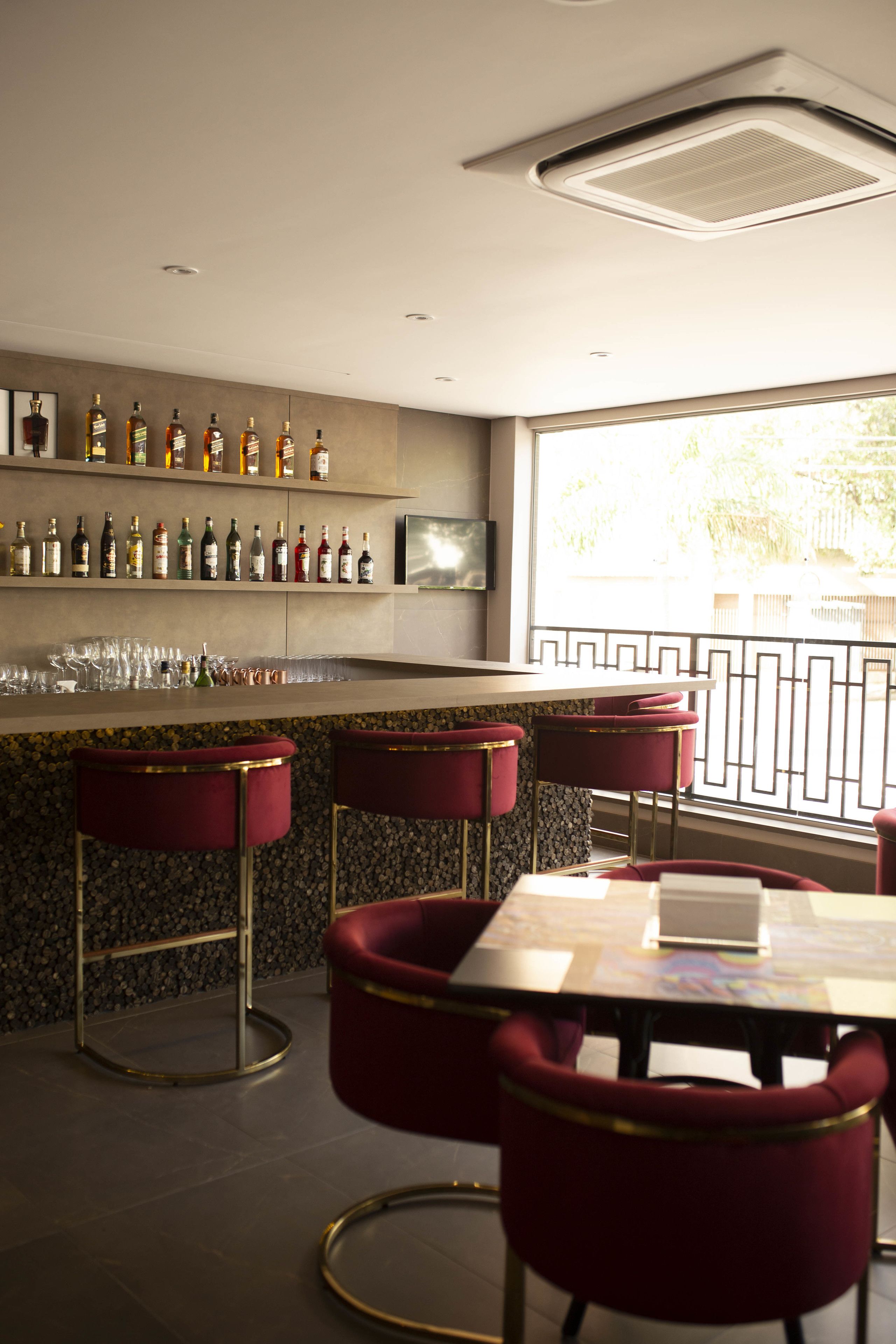 Uma área de bar com um balcão comprido, banquetas vermelhas e uma parede com garrafas de bebidas.