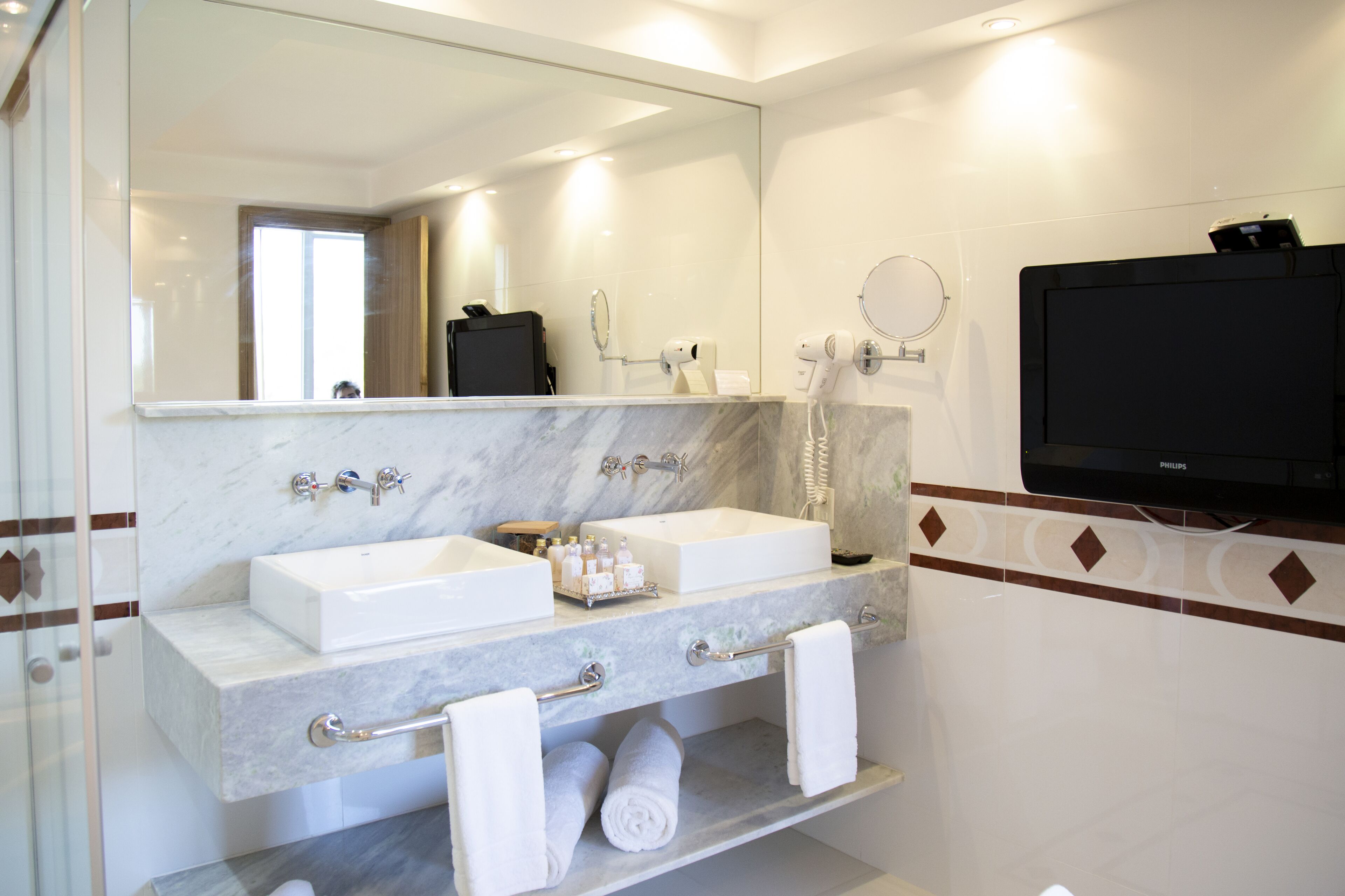 Un baño moderno con dos lavamanos, un espejo, un perchero para toallas y un televisor.