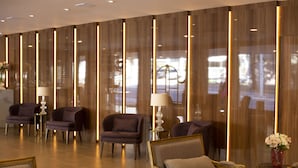 A modern lobby with seating areas, a reception desk, and a large window providing a view of the outside. - Hotel Florença (Americana)