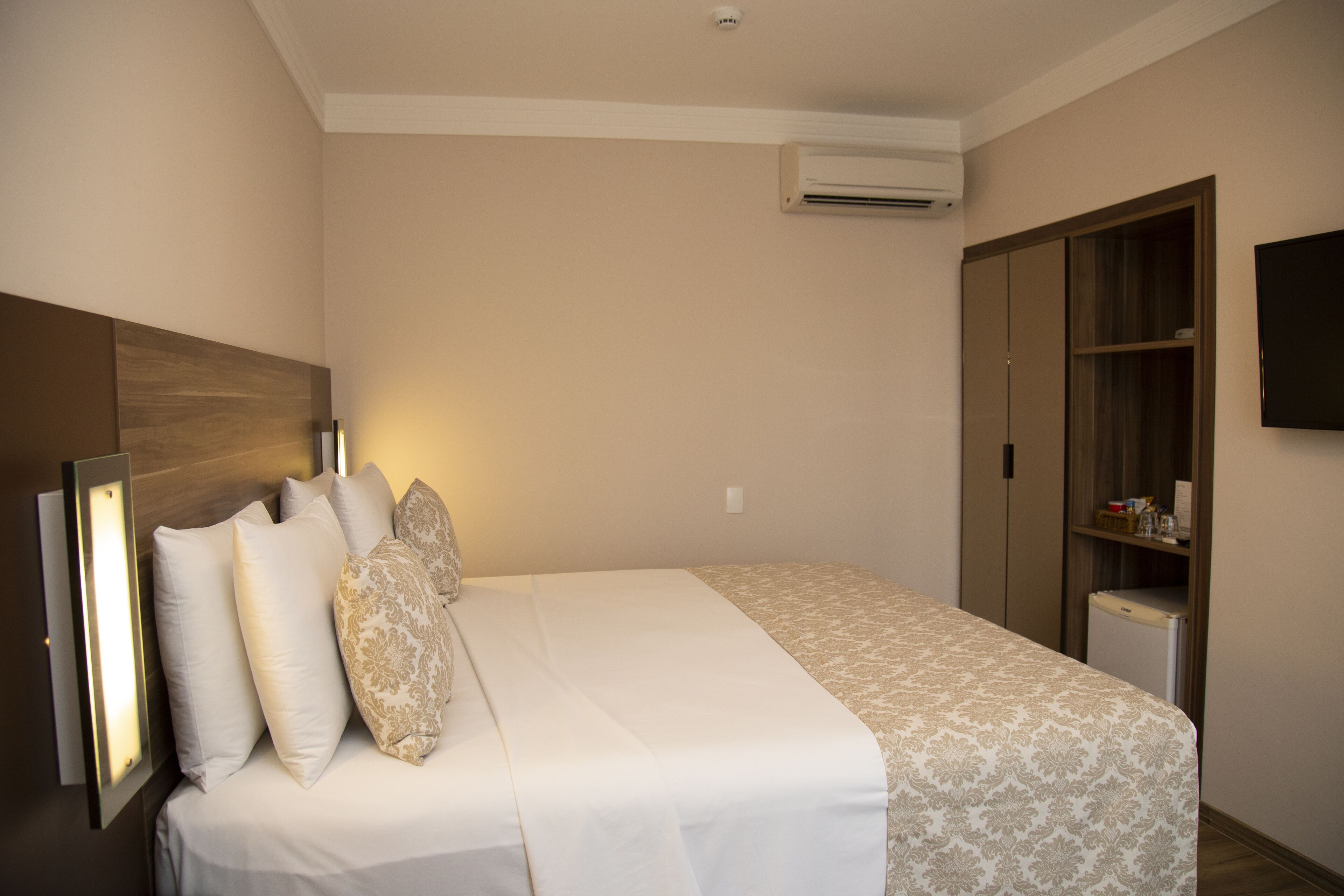 Ein Hotelzimmer mit Bett, Nachttischlampe, Kleiderschrank und Flachbildfernseher.