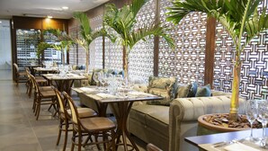 A restaurant with long tables, chairs, and a sofa. There are potted plants and a decorative wall. - Hotel Florença (Americana)