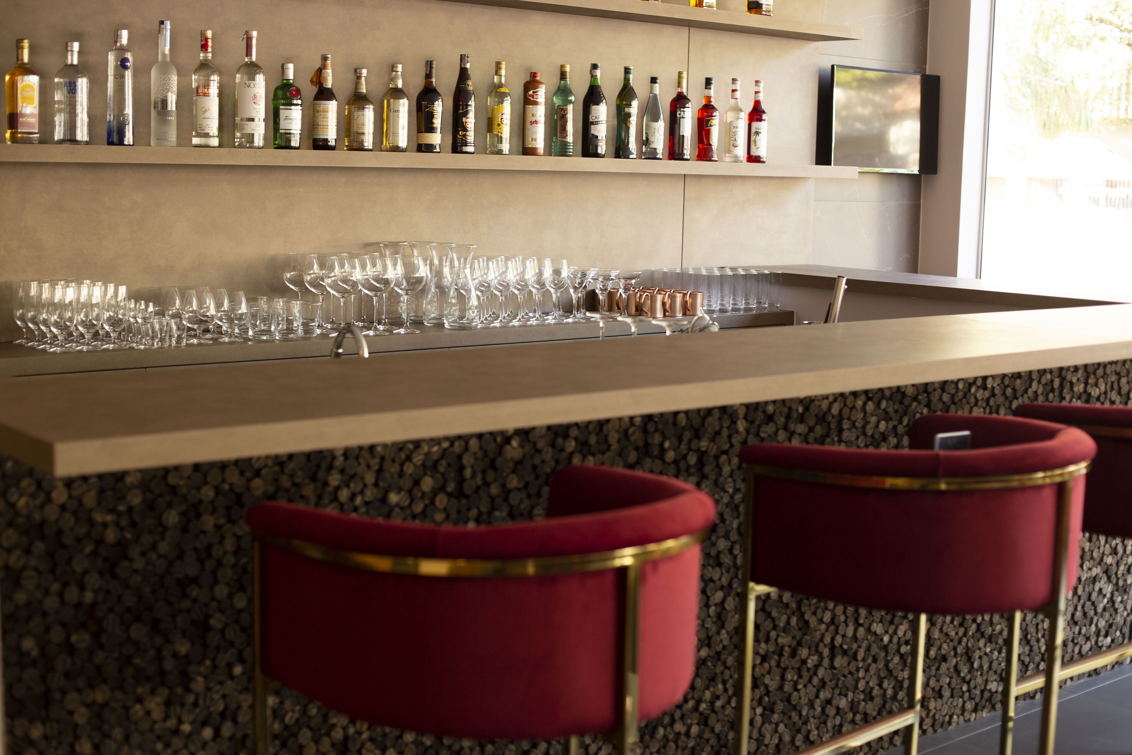 Uma área de bar com um balcão comprido, várias garrafas de bebidas alcoólicas e diversos copos e canecas.