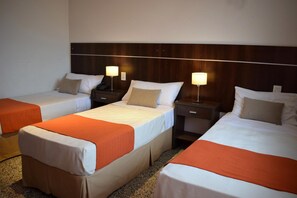 A hotel room with three single beds, each with a wooden headboard, white bedding, and an orange throw blanket. There are bedside tables with lamps and a small drawer. - Ref Apart Hotel (Salta)