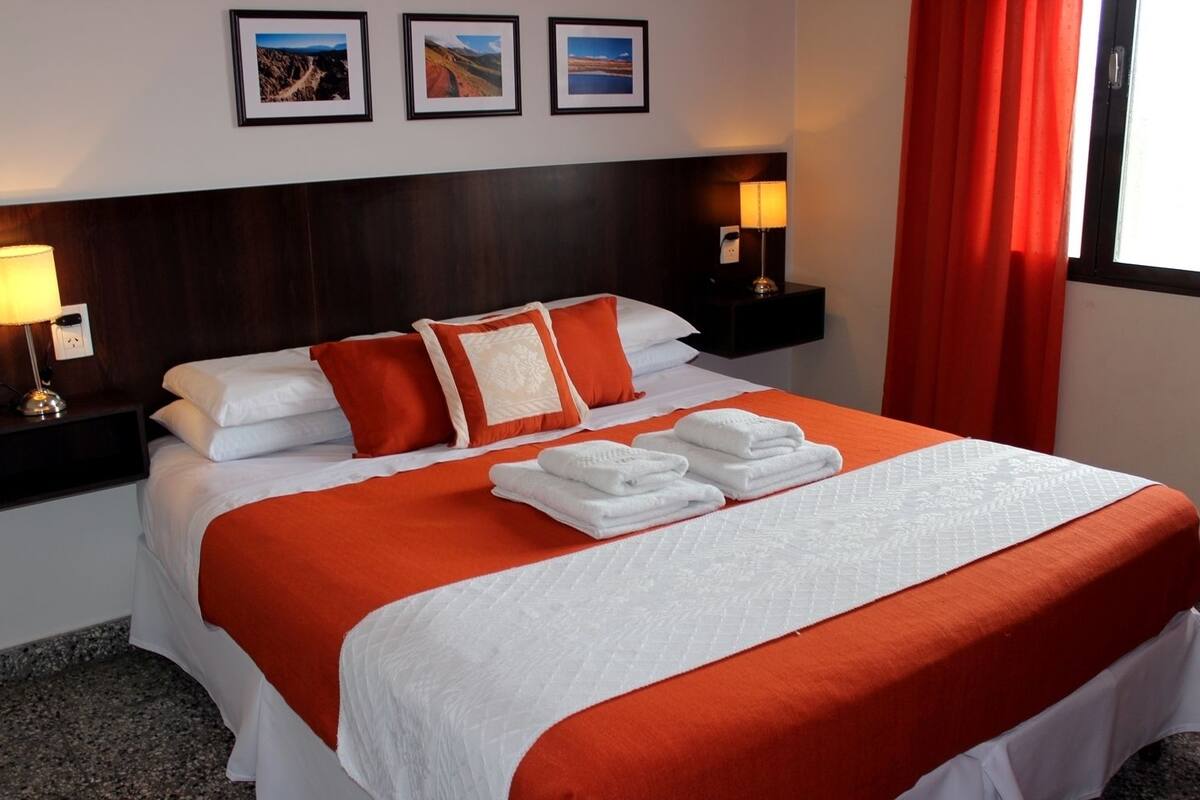 A neatly made bed with white and orange bedding, two bedside lamps, and three framed pictures on the wall.