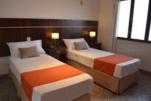 A hotel room with two beds, each with a white bedspread and an orange blanket. There are bedside tables with lamps and a wooden headboard. - Ref Apart Hotel (Salta)