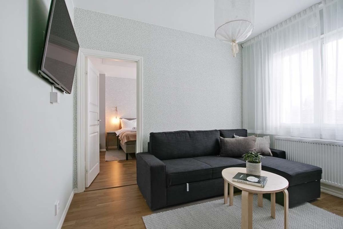 Un salon moderne avec un canapé gris foncé, une table basse ronde et un téléviseur fixé au mur.