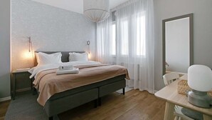 Ein modernes Schlafzimmer mit einem großen Bett, Nachttischlampen, Holzboden, einem Schreibtisch mit Lampe und einem großen Spiegel.