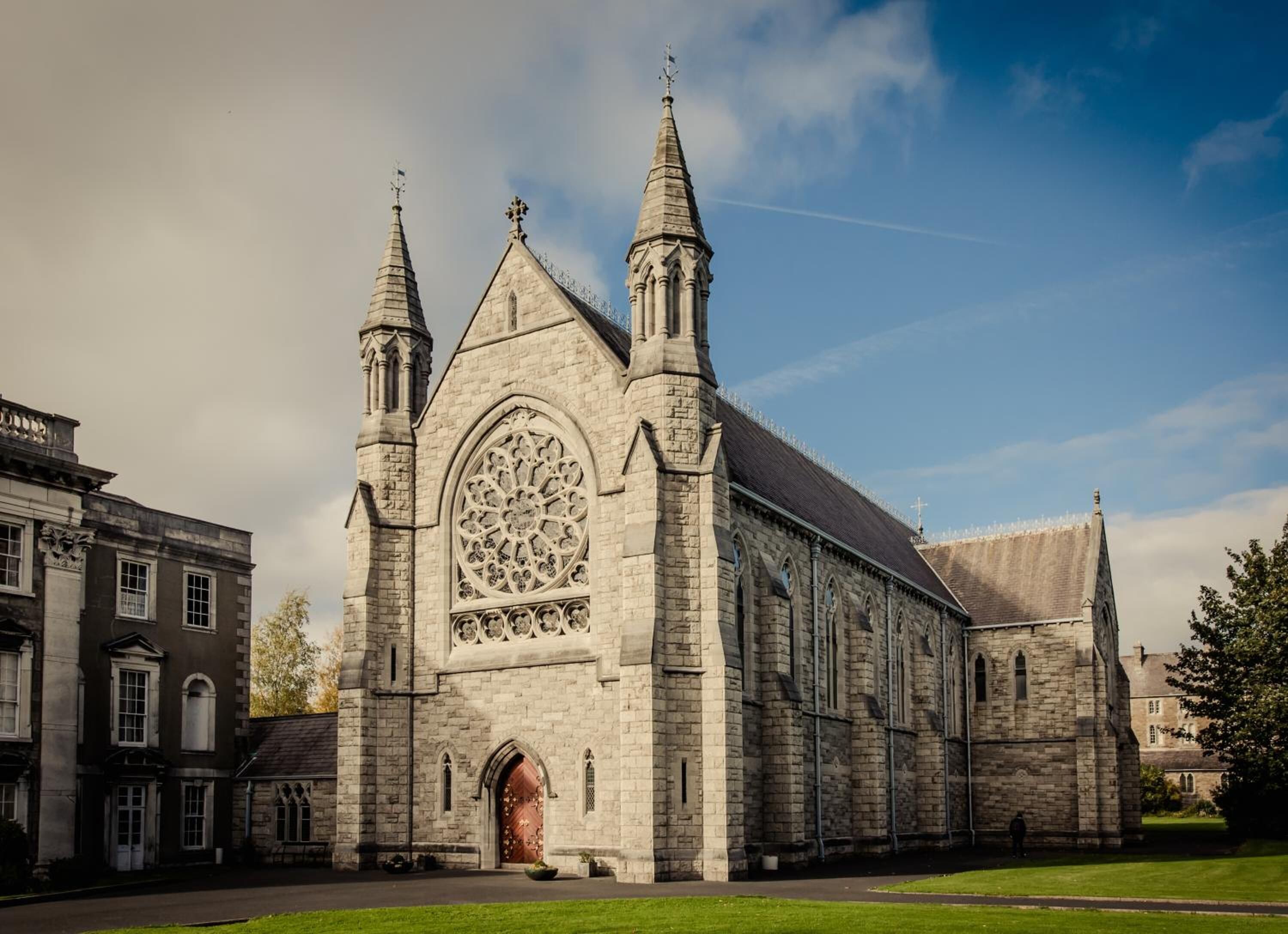 A large stone church with two spires, a large arched window, and a red door.