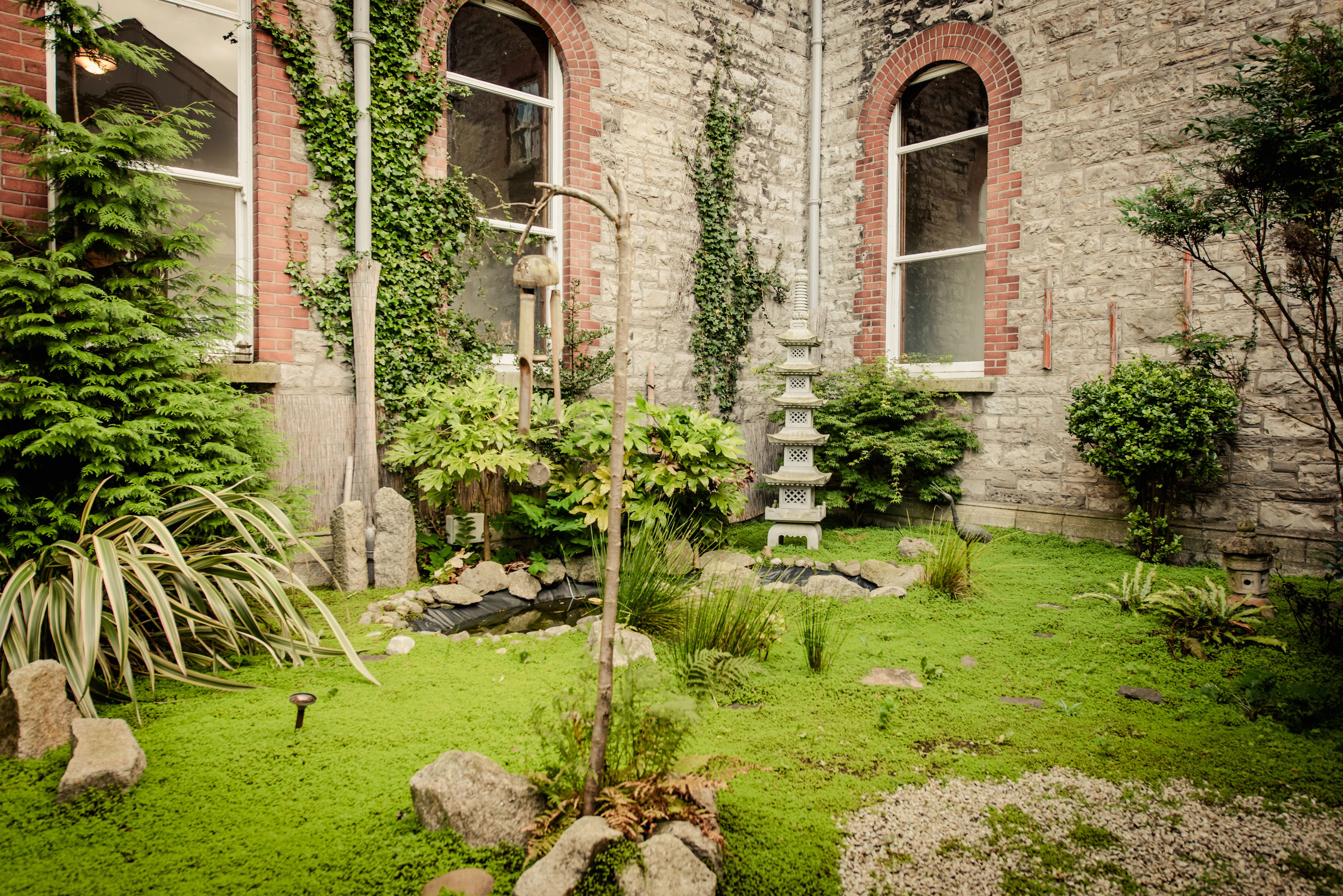 A garden with a stone wall, a small pond, and a traditional Japanese pagoda.