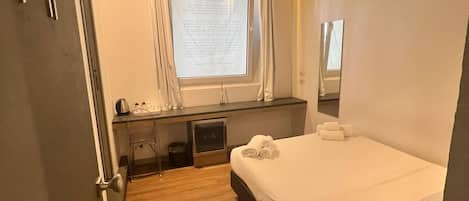 Una habitación de hotel moderna con una cama grande, un escritorio con silla, una ventana pequeña con cortinas y un espejo en la pared.