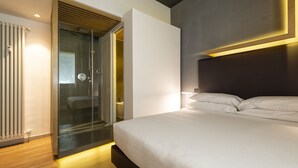 Una habitación de hotel moderna con una cama grande, cabina de ducha de vidrio y diseño minimalista.