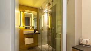 Un baño moderno con ducha de vidrio, tocador con espejo y hervidor sobre la encimera.