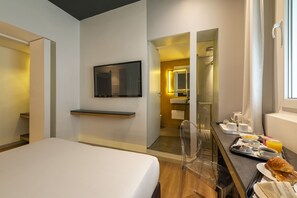 Een moderne hotelkamer met een bed, een bureau met ontbijtartikelen, een televisie en een badkamer die door een open deur zichtbaar is.