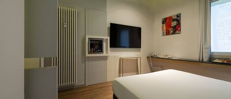 A modern hotel room with a large bed, a flat-screen TV mounted on the wall, a small table with a chair, and a radiator.