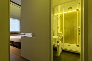 Een hotelkamer met een bed, een badkamer met een douchecabine van glas en een klein bureau met een computer.