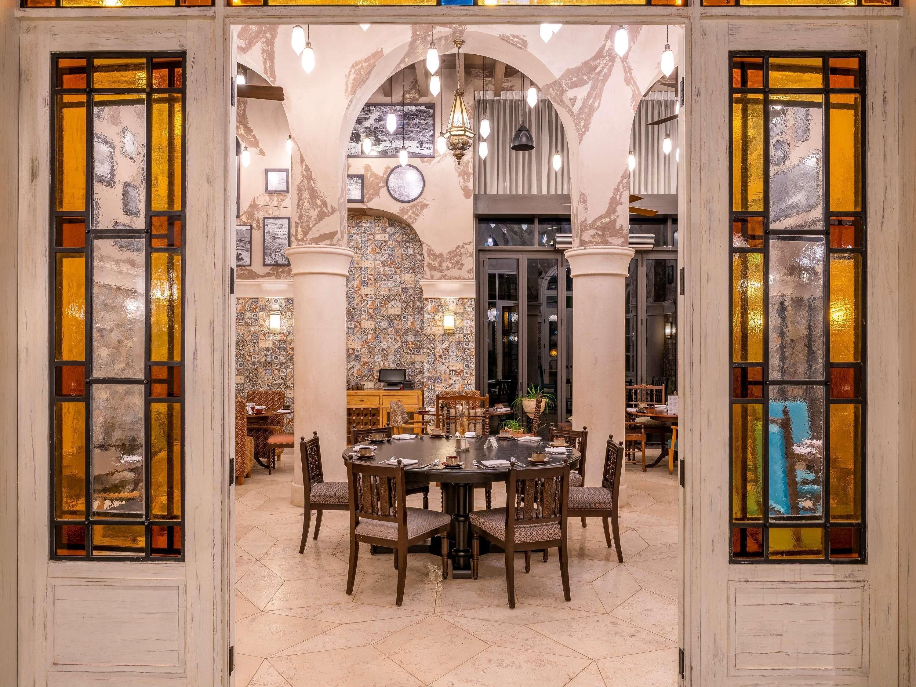 Un coin repas comprenant une table ronde, des chaises et une vue sur l’extérieur, visible à travers une porte en verre ornée de motifs.
