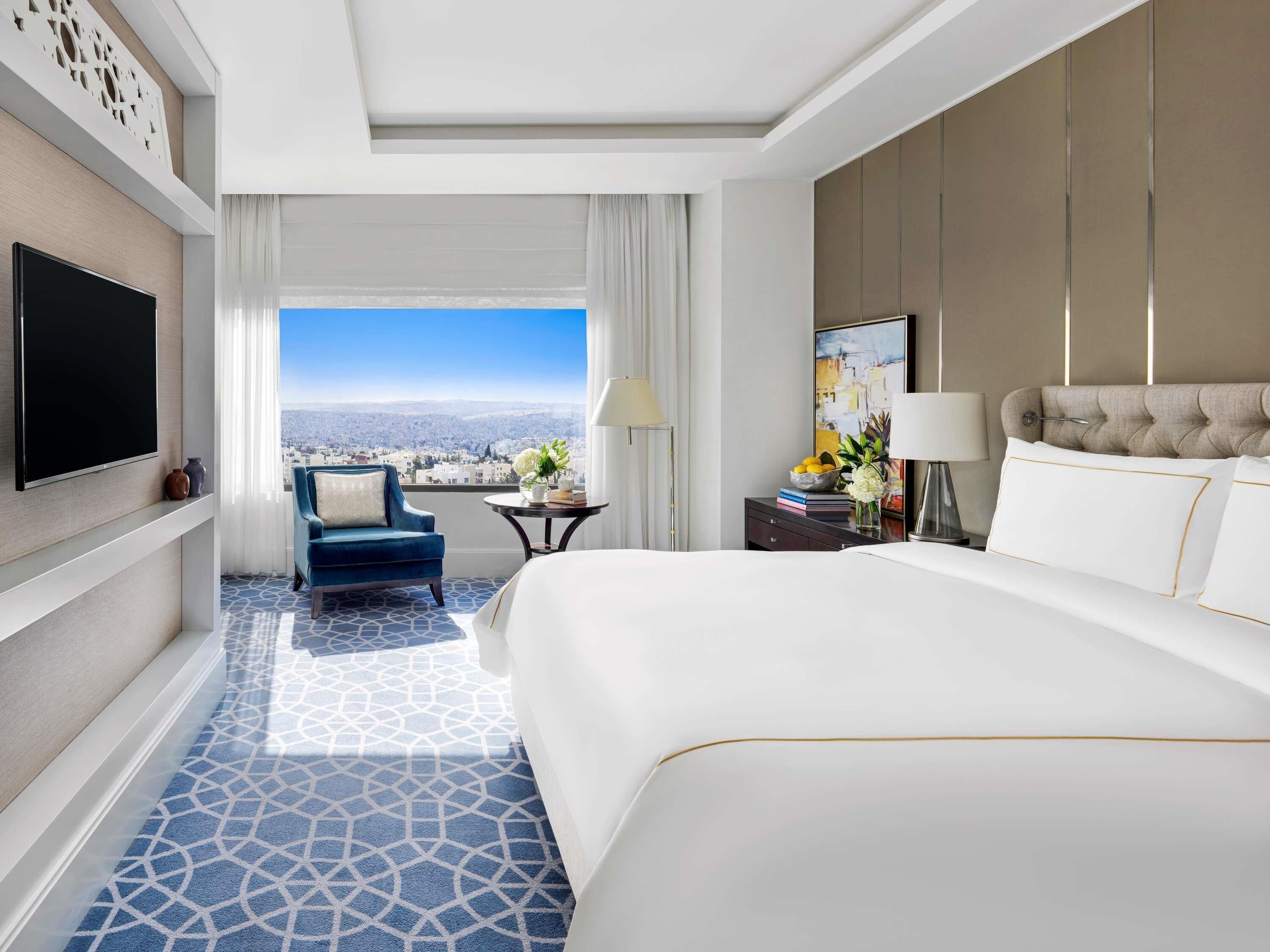 Une chambre d’hôtel avec un grand lit, une télévision, une chaise, une petite table et une vue sur la ville.