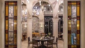 A dining area with a round table and chairs, surrounded by large windows with stained glass. - Fairmont Amman (Amman)