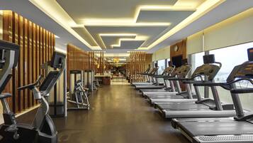 Une salle de sport équipée de plusieurs tapis de course, de vélos d’exercice et dotée d’un mur décoratif en bois.