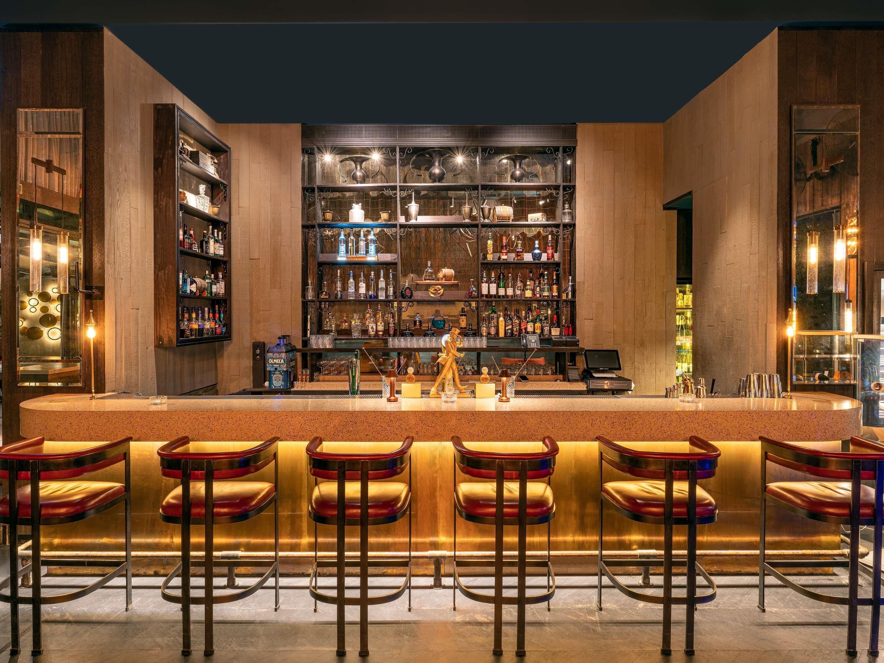 Un bar con una barra larga, varias estanterías llenas de botellas y taburetes.