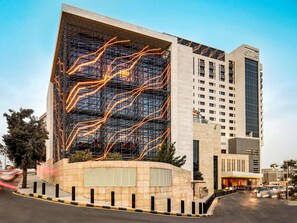 Un edificio moderno con una fachada distintiva de líneas iluminadas, una entrada destacada y una estructura alta contigua.