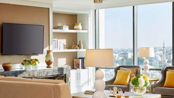 A modern living room with a flat-screen TV, a fireplace, a sofa, a coffee table, and a view of a cityscape through large windows.