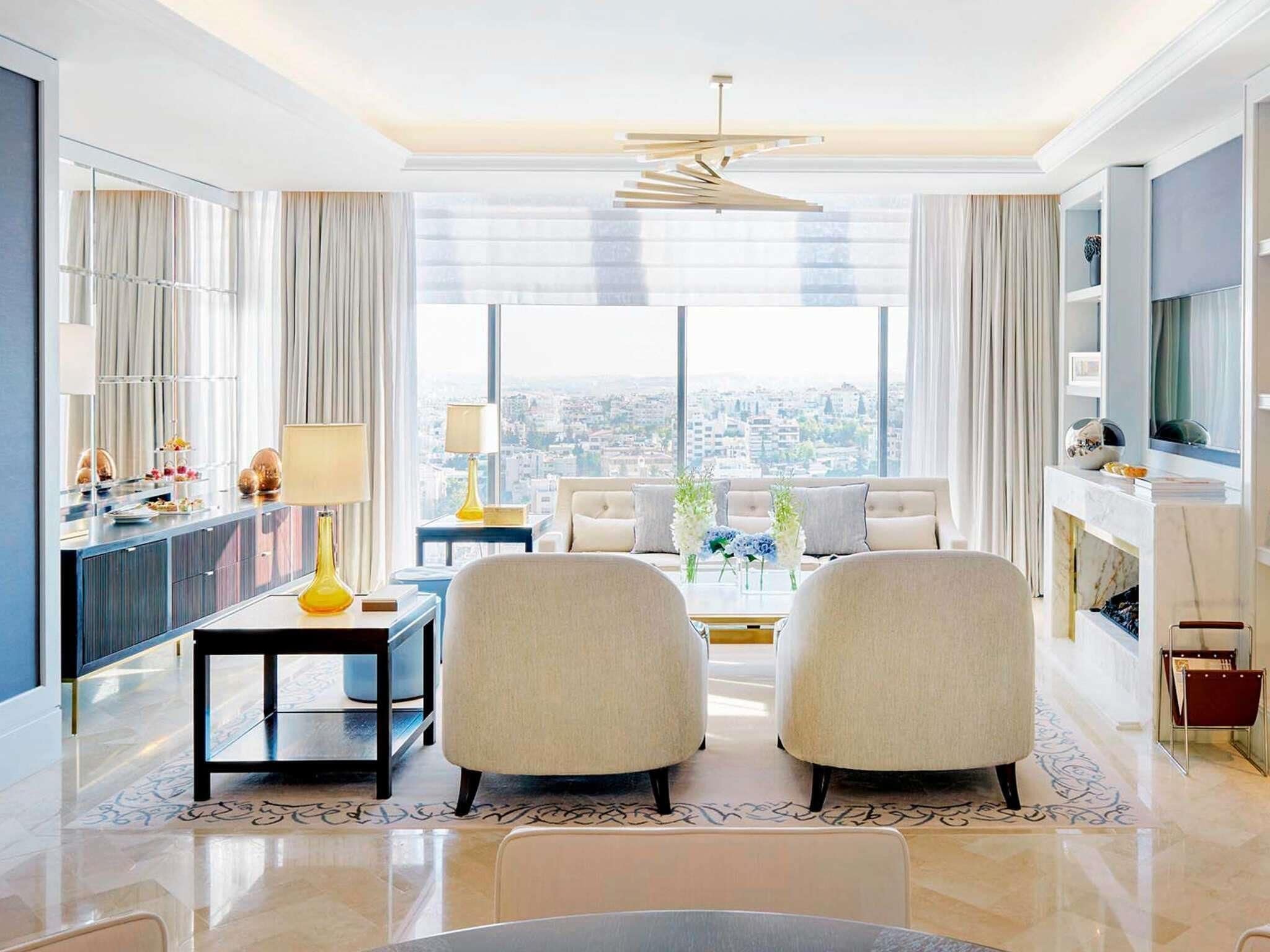Habitación de hotel moderna con vistas a la ciudad, zona de comedor y un área de estar con dos sillones.