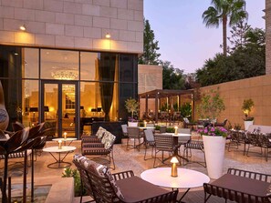An outdoor patio area with seating arrangements, a glass entrance, and a view of the interior. - Fairmont Amman (Amman)