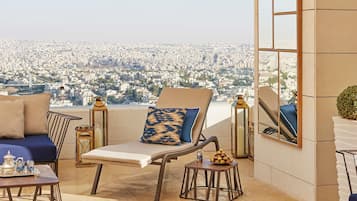 A balcony with a city view, a sofa, a chair, a small table with a tray, and a decorative lamp.