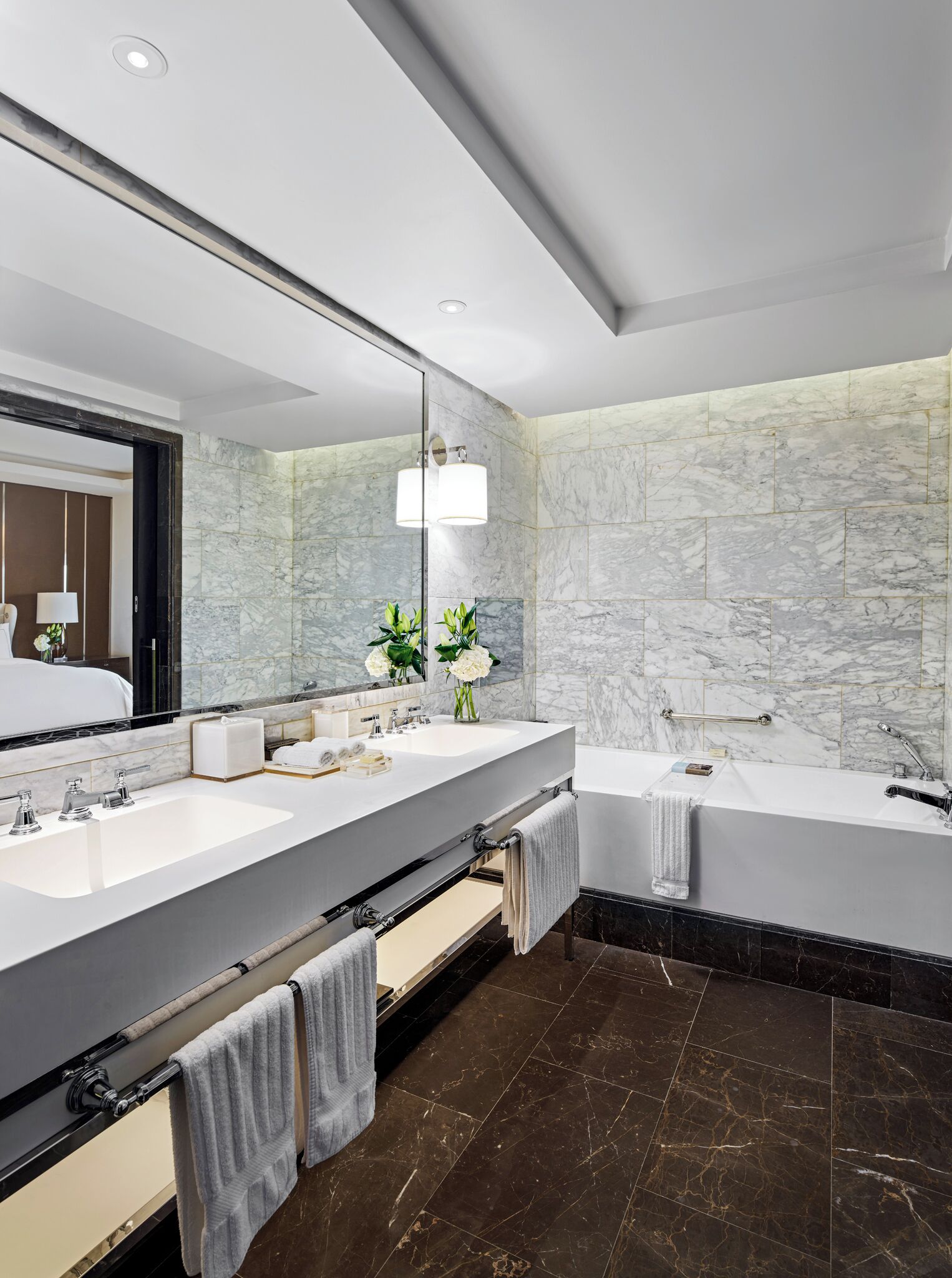 A modern bathroom with two sinks, a large mirror, a bathtub, and marble walls.